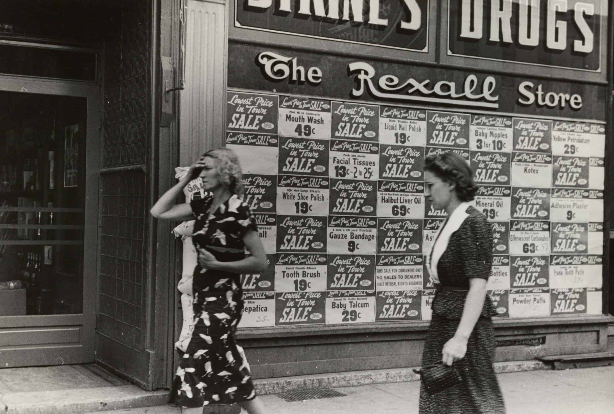 Vintage street scene with women walking past a store with sale signs.